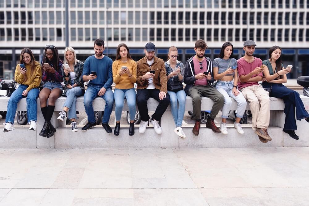 A Group Of Eleven Teenagers Sitting On A Wall